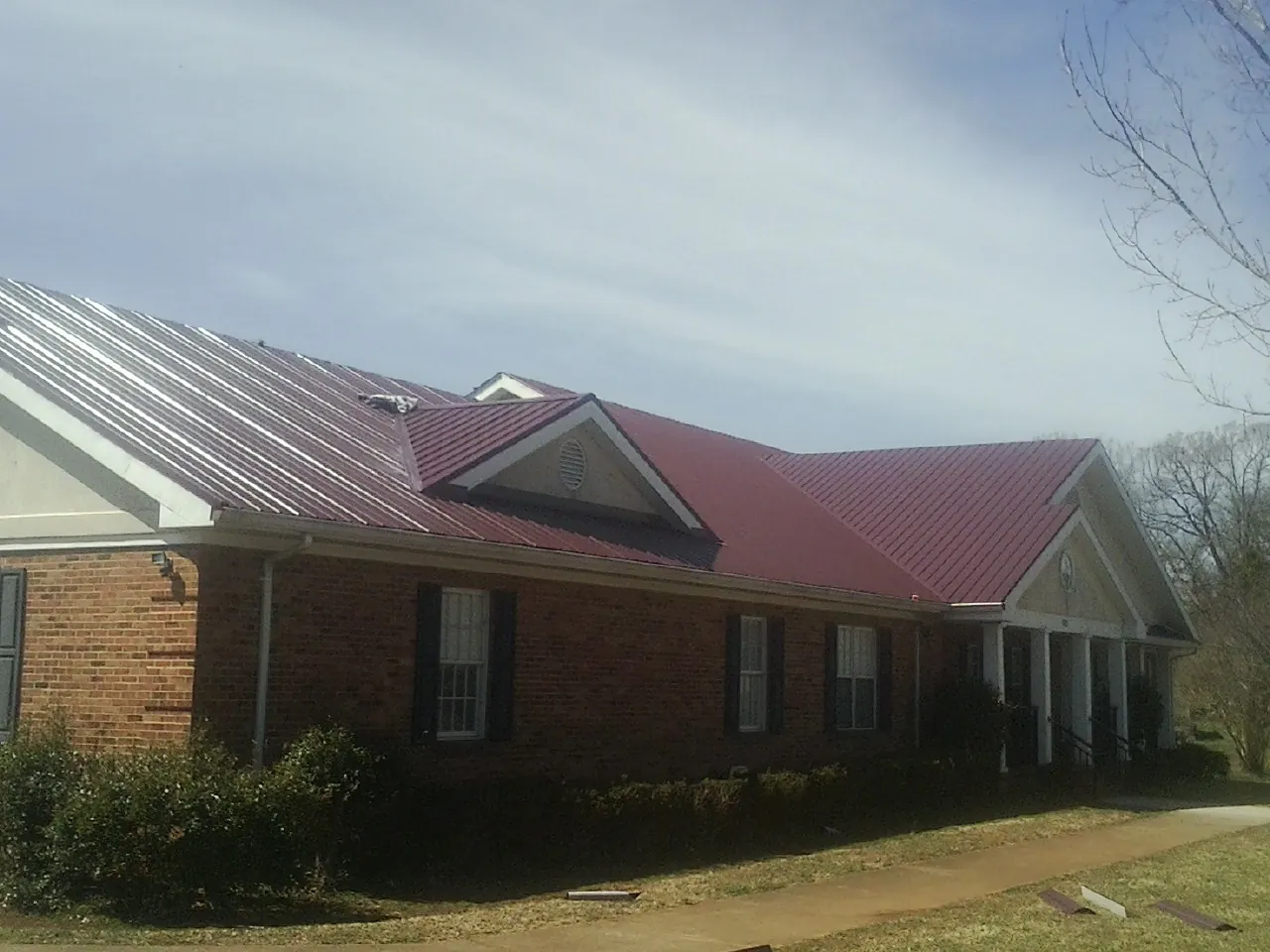 Red metal roof with gabled entries on a long brick building, from a Hail Damage Roof Repair job in Damascus