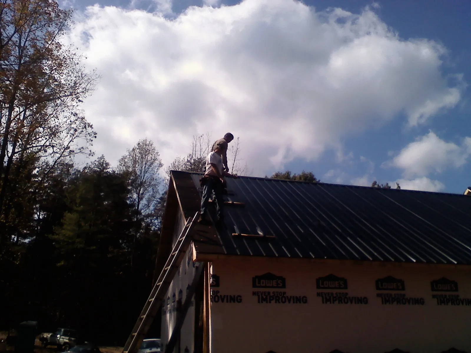 Roofer fastening dark metal panels high against a cloudy sky, from a Roof Inspection job in Damascus