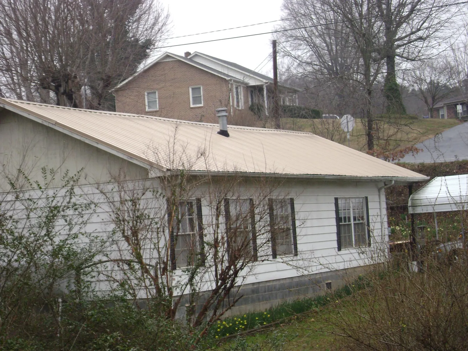 Tan metal roof on a white sided house set into a hillside — Commercial Roofing by Roofing Brothers in Damascus